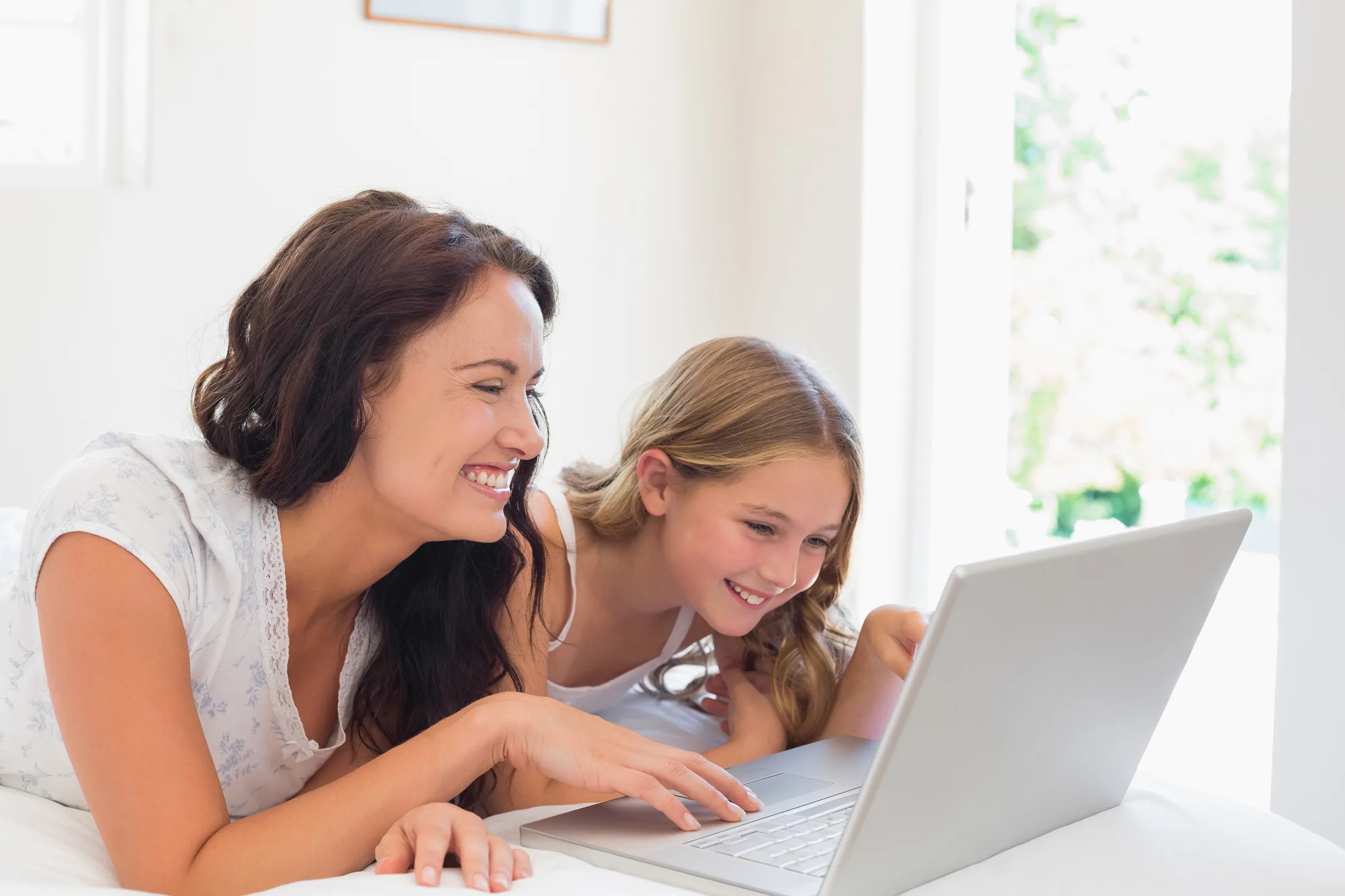 Internet familiar: Madre e hija sonriendo mientras usan su laptop conectada al Wi-Fi desde la cama.