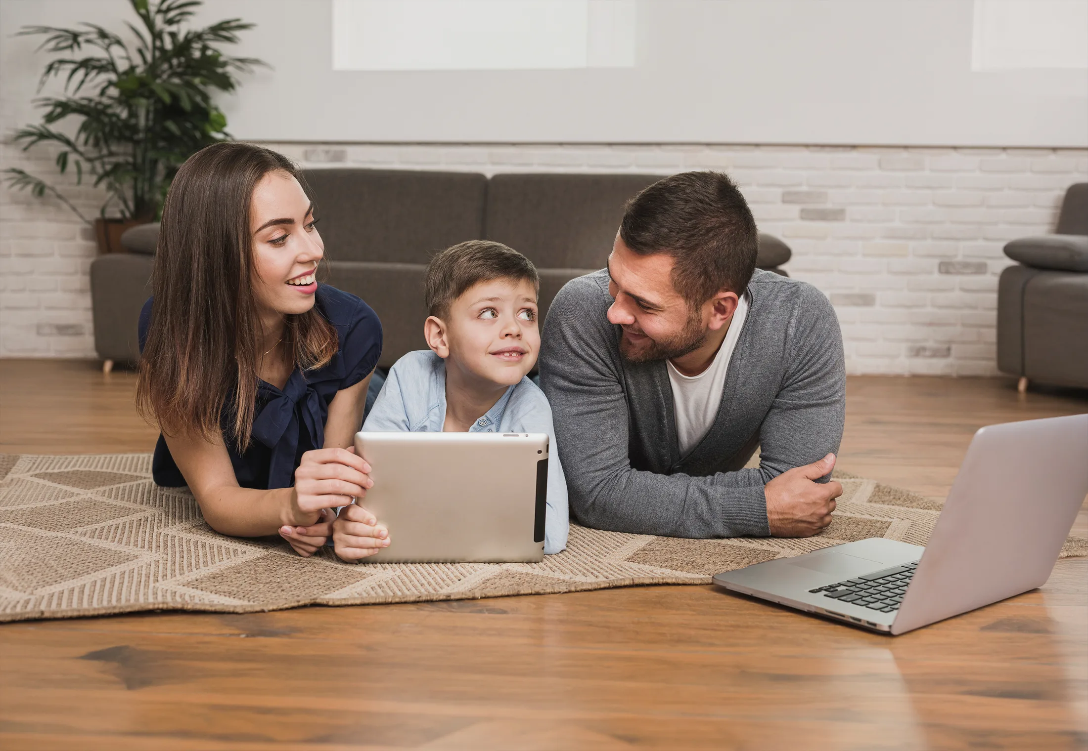 Internet familiar: Familia feliz en la alfombra usando una tablet y una laptop simultáneamente con Wi-Fi estable.
