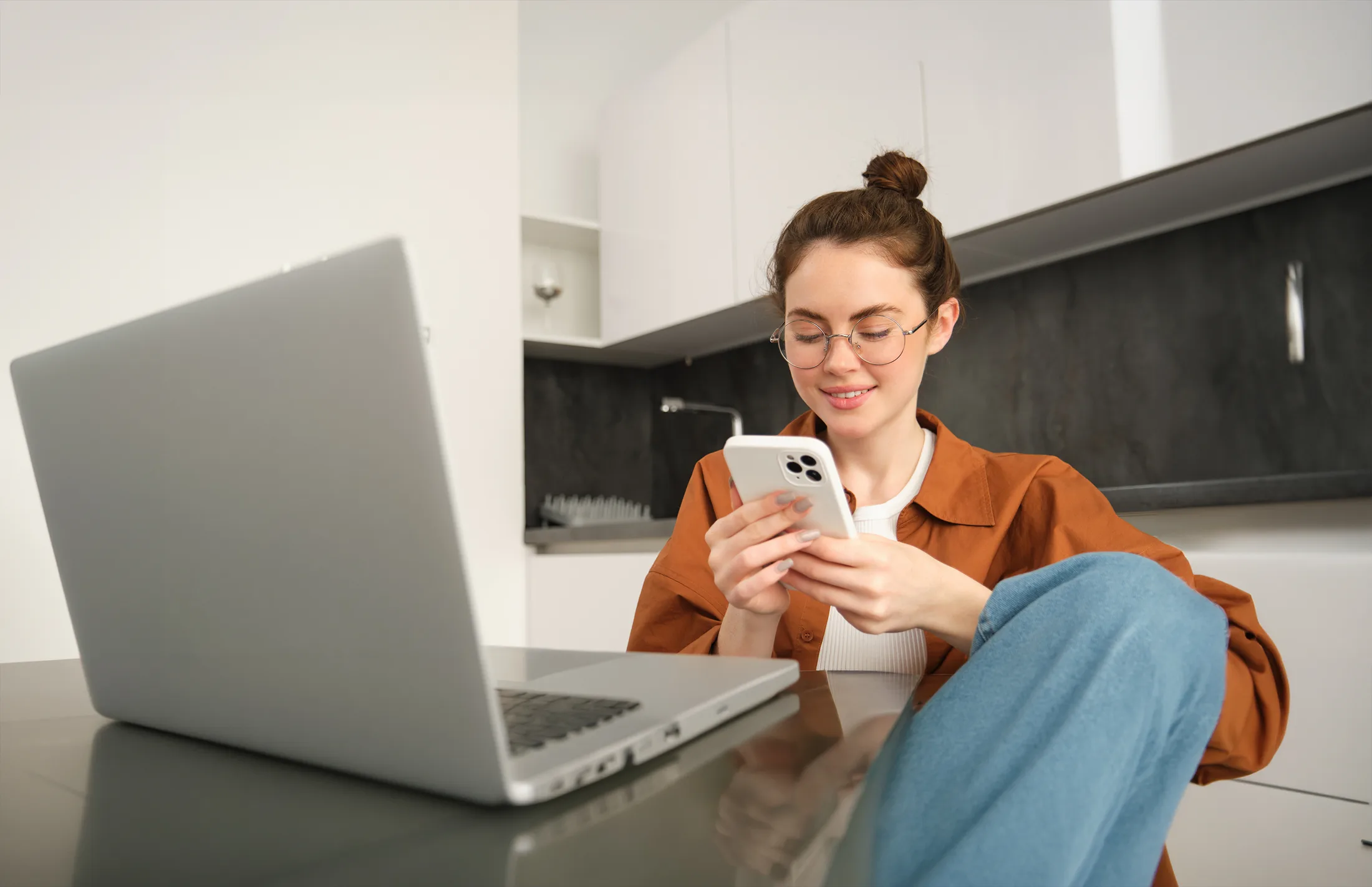 Work from home: Mujer sonriendo mientras revisa su smartphone junto a una laptop conectada al Wi-Fi.