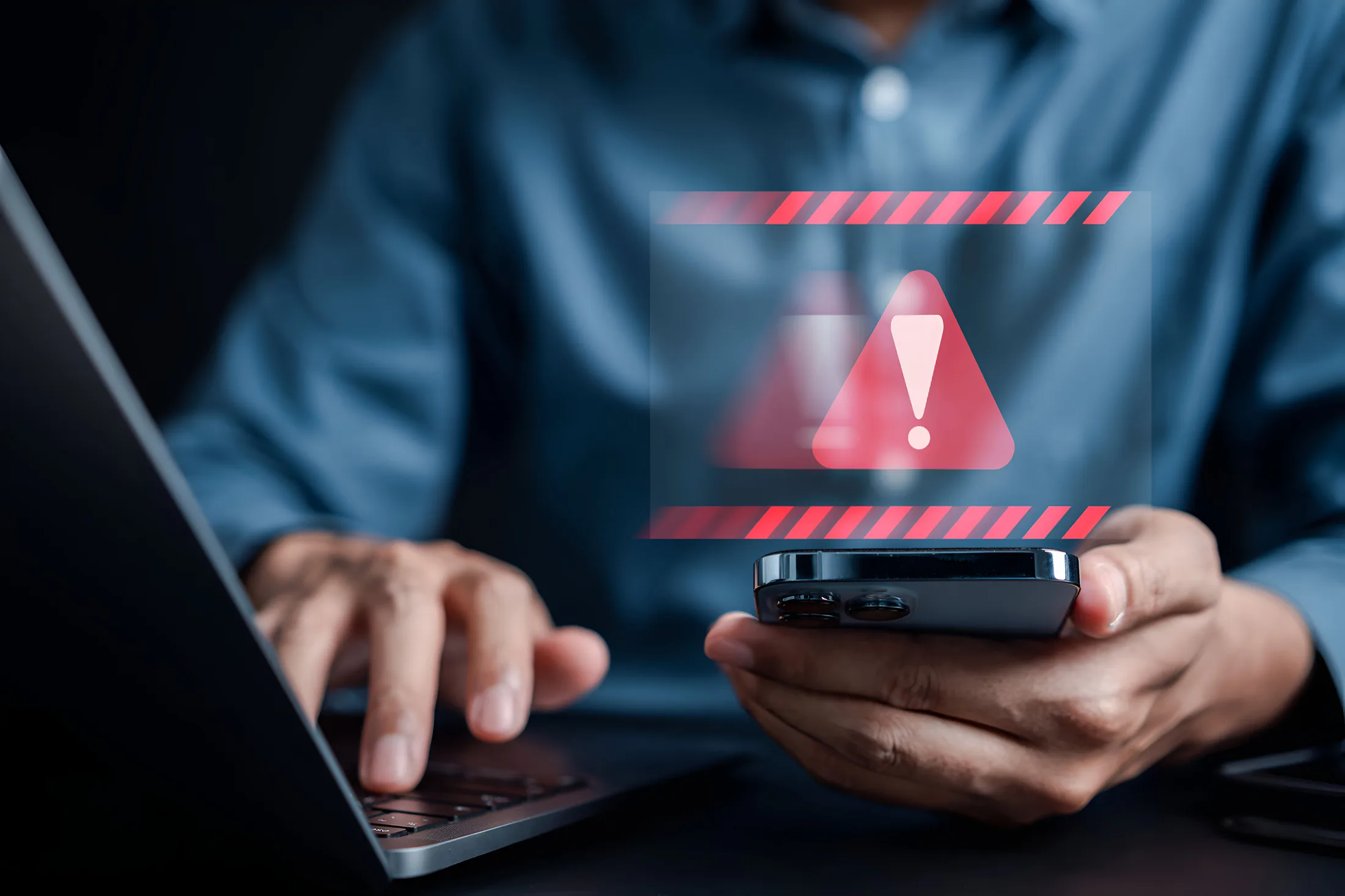 Seguridad online: Alerta roja de ciberseguridad en el smartphone de un usuario trabajando en su laptop.