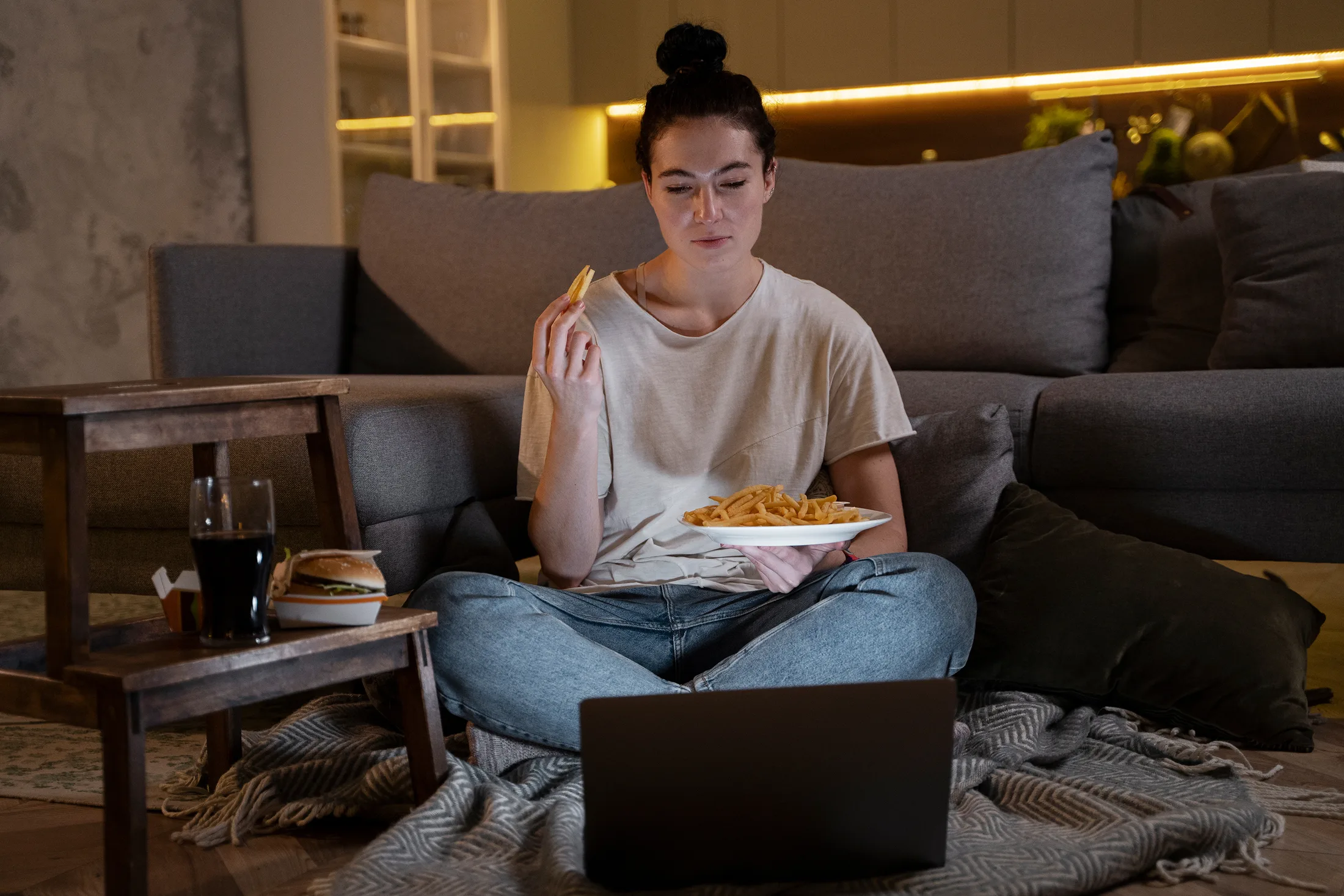 Streaming nocturno: Mujer relajada comiendo mientras ve contenido online en su laptop sin interrupciones.