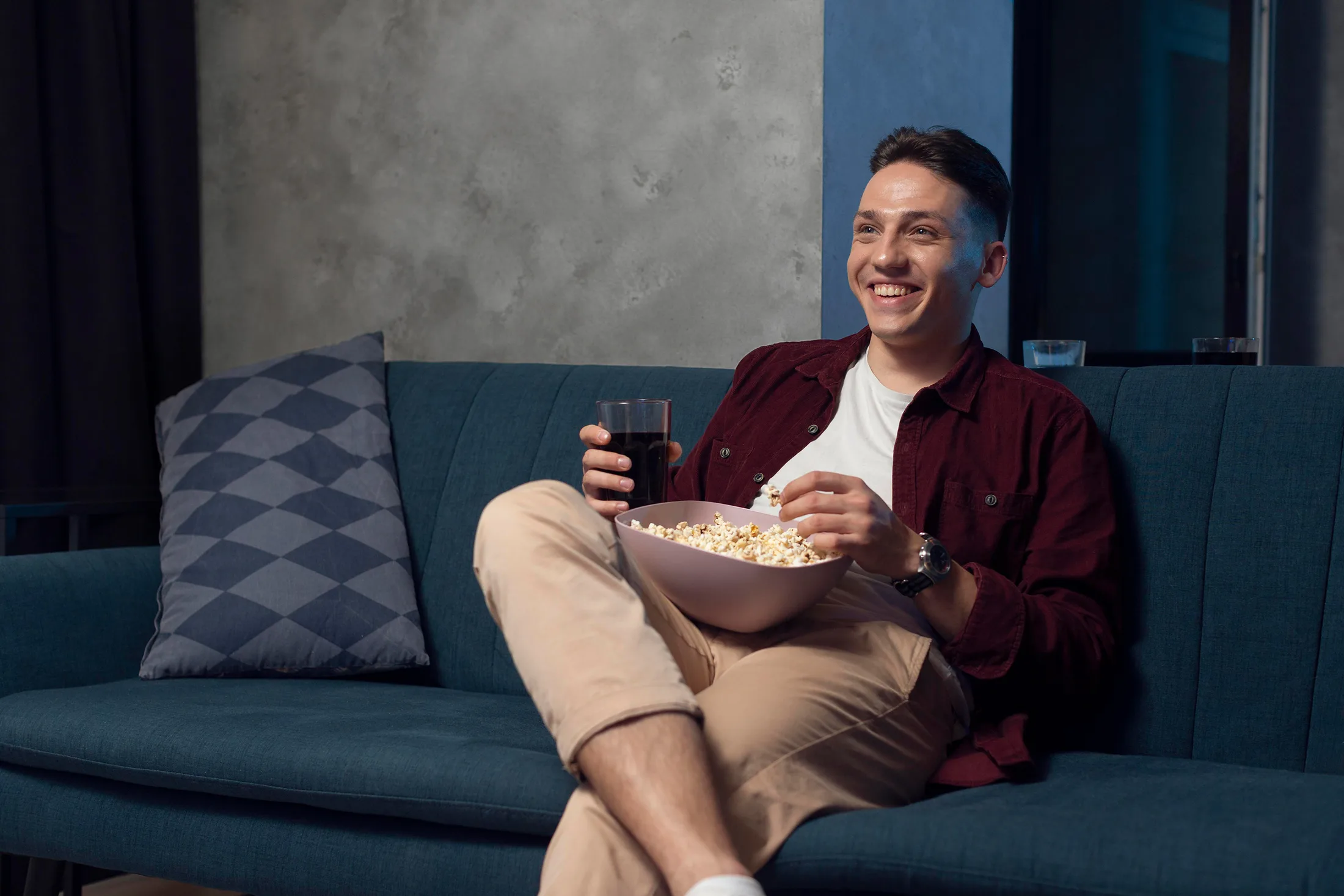 Streaming sin lag: Hombre sonriendo en el sofá con palomitas disfrutando de una película online.