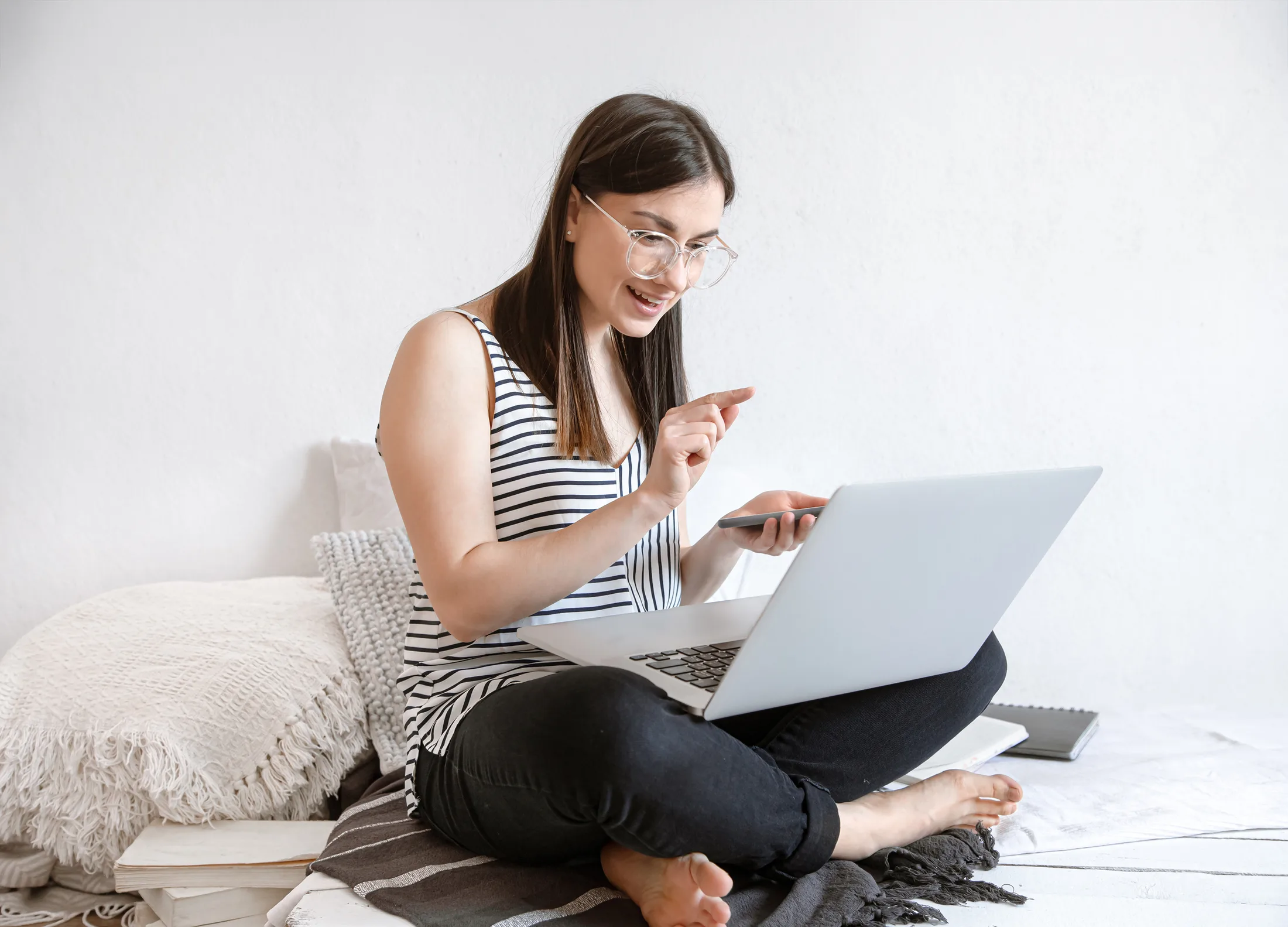 Work from home: Mujer sonriendo mientras hace multitasking con su laptop y smartphone conectados al Wi-Fi.